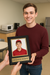 Man holding a framed photo of himself with 'Employee of the Month' text in an office setting.