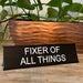 Fixer of all things funny office desk plate in front of a plant.