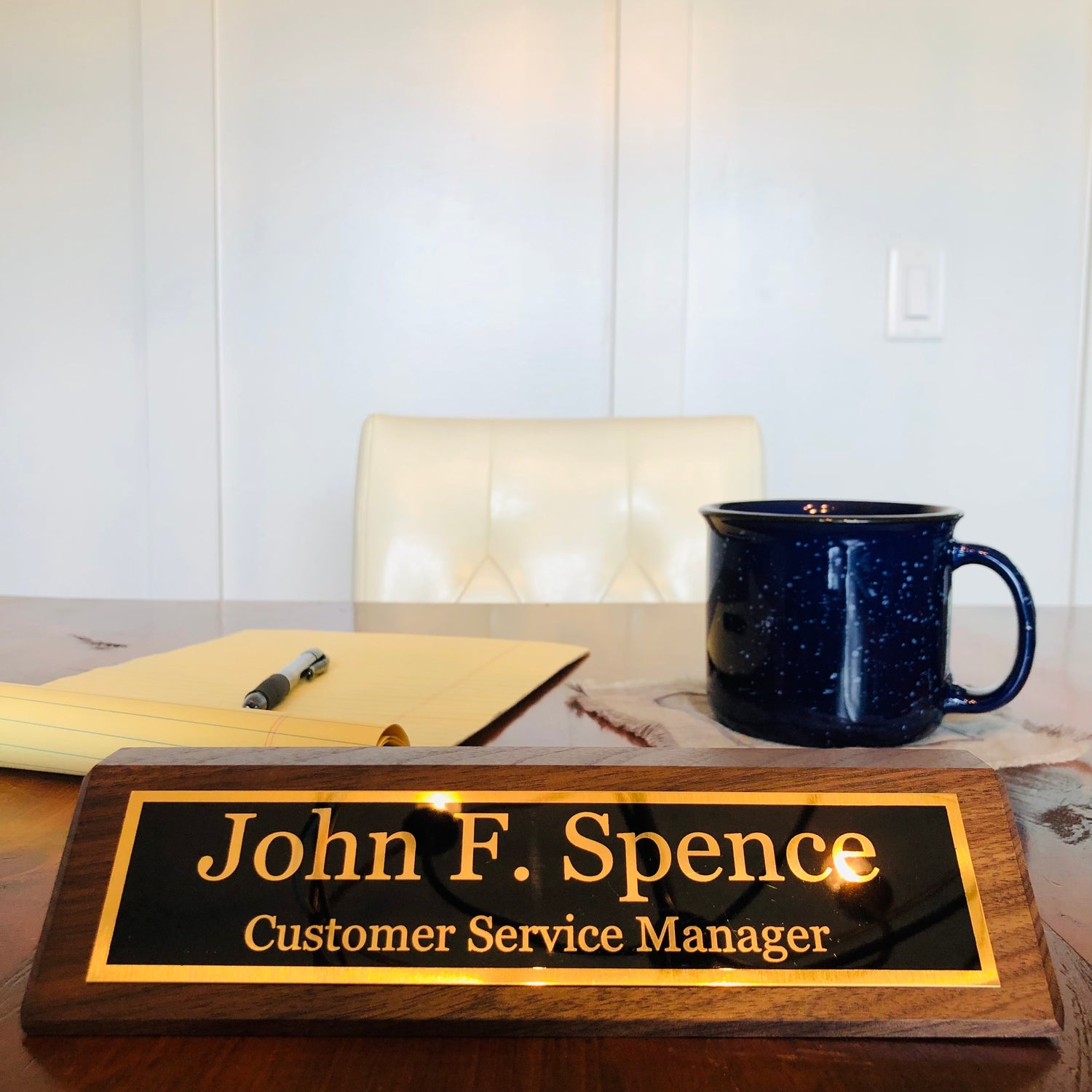Close up view of walnut name plate on desk with coffee mug and legal pad.