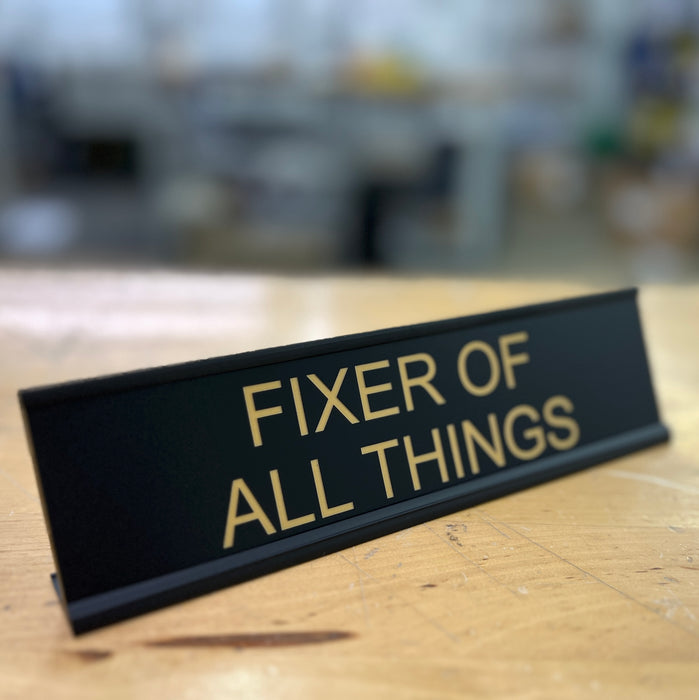 Fixer of all things desk sign sitting on top a dek in a warehouse.